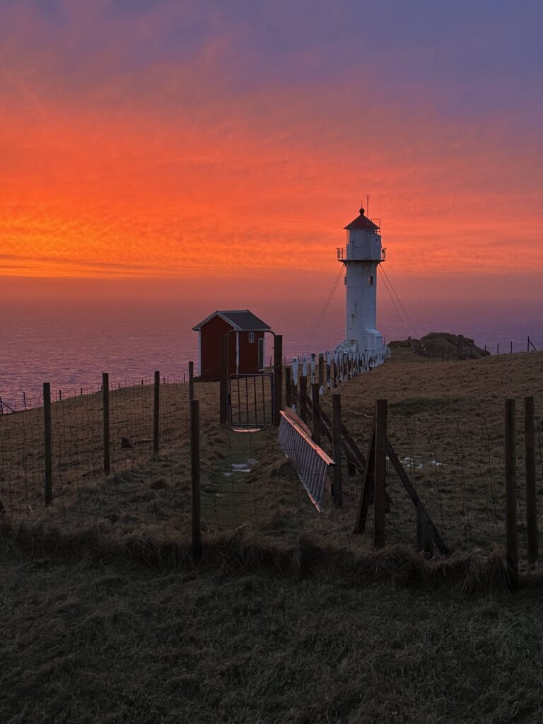 Fiery red and orange sunset with Akraberg lighthouse and fence path silhouetted