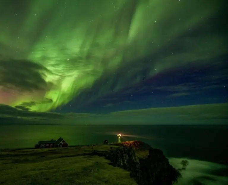 Stunning aurora borealis over the Akraberg headland with lighthouse glowing below