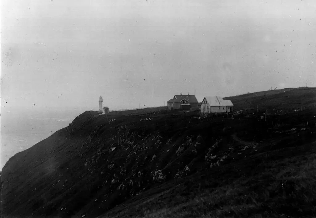 Historical black-and-white photograph of Akraberg lighthouse and keeper's buildings on the headland